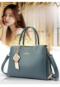 Détail du sac à main bleu-gris profond avec logo doré et pendentif en métal tressé