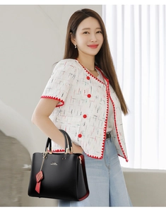 Détail d'un sac à main en cuir noir avec des touches rouges et un logo métallique