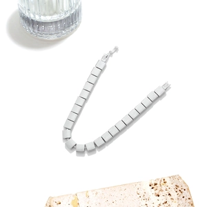 Detail of silver square link bracelet with matte metal finish and hidden clasp on white stone