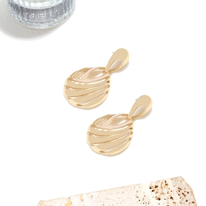 Detail of gold hollow geometric drop earrings with pearl accents on a stone pedestal