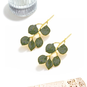 Macro detail of long green enamel leaf earrings with elegant golden metal branches