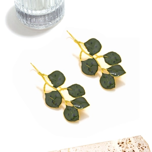Detail view of handmade green enamel leaf earrings on a minimalist stone background