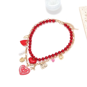 Detailed view of layered necklace with red beads, gold charms, hearts and leaf pendants