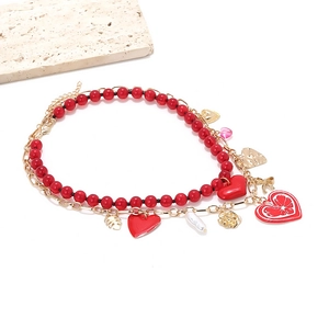 Layered gold chain necklace with red heart pendants, pearls and leaves on white background