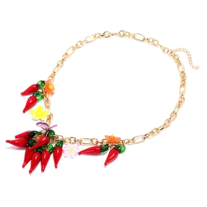 Collier doré avec pendentifs piments rouges et fleurs colorées sur fond blanc neutre