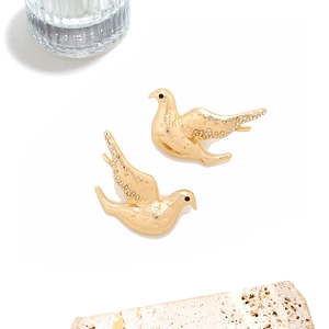 Détail de boucles d'oreilles oiseaux dorés avec ailes pavées et texture métallique ciselée