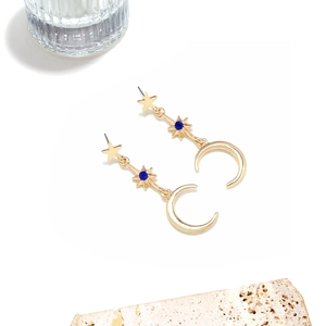 Detail of gold moon and star drop earrings with blue crystals on white background