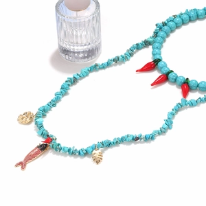 Detail of turquoise beaded necklace with red chili pendant and golden charms on white