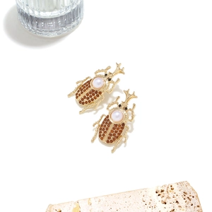 Detail of gold beetle earrings with pearls and crystals on decorative stone background