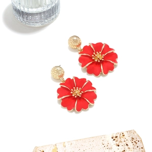 Gros plan de boucles d'oreilles fleurs en émail rouge avec pistils dorés sur pierre
