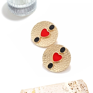 Close-up of vintage heart earrings featuring gold hammered texture and red enamel finish