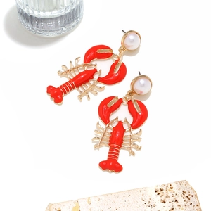 Close-up of golden lobster earrings with red enamel and white pearl accents on white stone