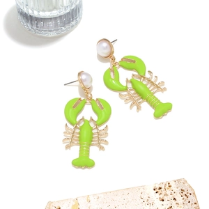 Detailed view of neon green lobster earrings with gold accents and pearls on a stone base