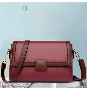 Detailed close-up of burgundy crossbody bag with lychee grain texture and gold metal buckle