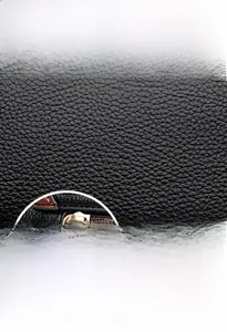 Detail of black lychee grain leather handbag with brown edges and gold-tone hardware