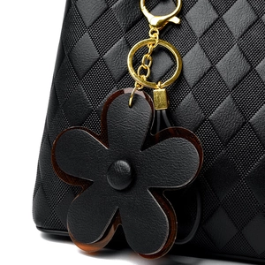 Détail du charm fleur dorée sur un sac à main noir matelassé avec finitions métalliques