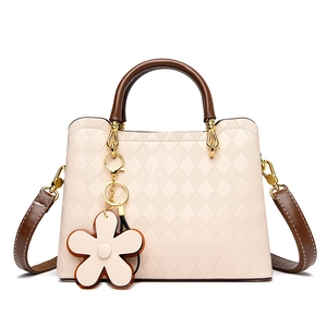 Détail du sac à main à motif losanges avec poignée marron et breloque fleur sur fond blanc