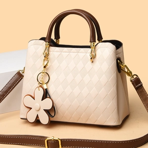 Détail d'un sac matelassé beige avec poignées marron et charm fleur dorée
