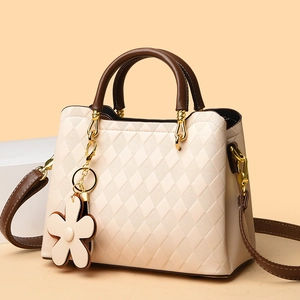 Détail du sac matelassé crème avec poignées marron et breloque fleur sur fond orange