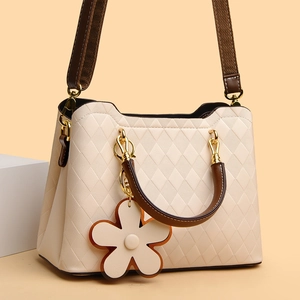 Détail du matelassage en losange sur sac crème avec boucles dorées et breloque en fleur