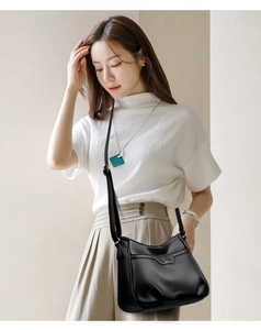 Detail of black crossbody bag with lychee texture shown on a female model