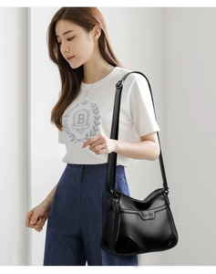 Model wearing black litchi pattern leather crossbody bag with embossed logo detail