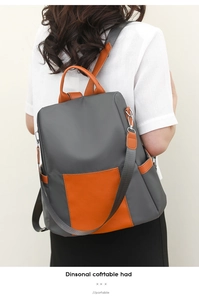 Detail view of the gray and orange contrast backpack featuring leather handle and side pocket