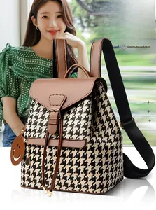 Detail of houndstooth backpack featuring brown leather flap and smiling face charm