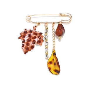 Broche épingle dorée avec pendentifs feuille léopard et perles sur fond blanc