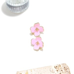 Close-up of pink enamel flower stud earrings with golden plating on a white stone base