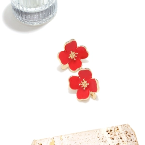 Detail of red enamel flower earrings with gold-plated edges on a stone tray