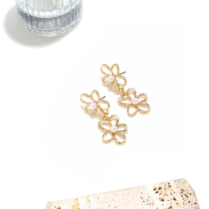 Detail view of gold layered flower earrings with faux pearls on a stone pedestal