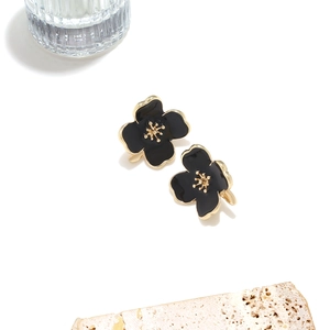 Macro detail of black enamel flower earrings with gold petals and 3D textured core