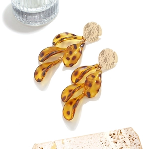 Detail of layered gold metal and amber leopard leaf drop earrings on stone