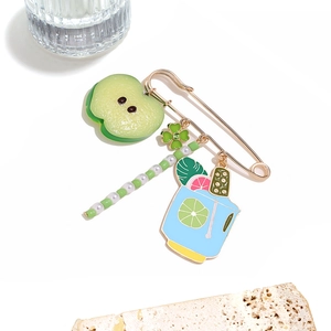 Detail view of summer drink brooch with green apple, clover, and pearl charms on gold pin
