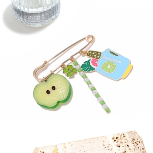 Detailed view of apple and wine glass charms on a golden safety pin brooch with green beads