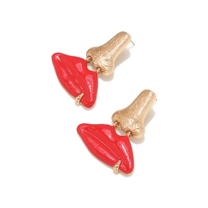 Détail macro de boucles d'oreilles surréalistes avec nez doré et lèvres émaillées rouges