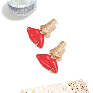 Détail de boucles d'oreilles nez doré et lèvres émaillées rouges sur socle en pierre