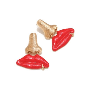 Détail de boucles d'oreilles créatives avec nez doré et lèvres en émail rouge sur blanc