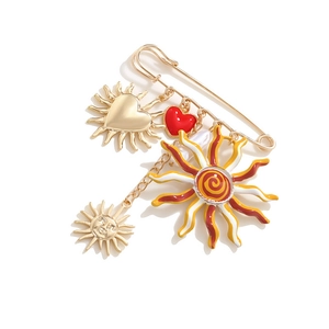 Golden paperclip brooch featuring sun and red enamel heart charms on a white background