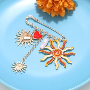 Detailed view of a gold brooch pin with sun heart charms and pearl on a blue tray
