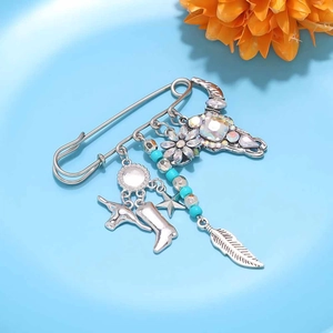 Detail of silver safety pin brooch with cow head, denim boot and feather charms
