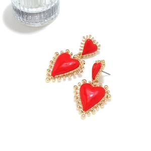 Detalle de pendientes de corazón de esmalte rojo con bordes de cuentas doradas