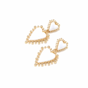 Detalle de pendientes de corazón dorados con esmalte blanco y bordes de cuentas finas