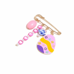 Golden Easter egg brooch with pink heart beads and floral charms on white background