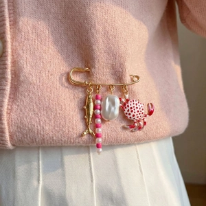 Brosche mit buntem Krebs und Fisch auf rosa Strickjacke mit eleganten Perlen