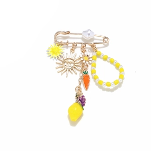 Exaggerated brooch with sun, lemon, daisy, and carrot charms on a gold safety pin