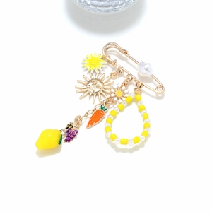 Detailed view of charms including lemon and daisy on a golden safety pin brooch