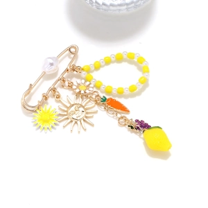 Detail of creative brooch featuring lemon, carrot, and daisy charms on a golden pin