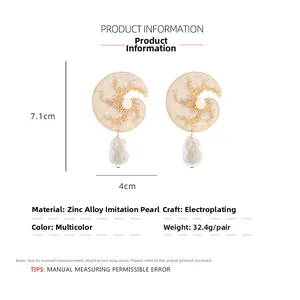 Detail of gold shell drop earrings with baroque pearls and textured finish on white base